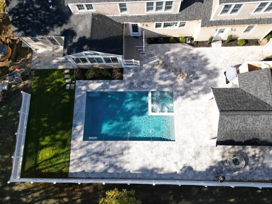 Aerial view of a fenced travertine patio with a pool and corner spa in Harwich Port, MA