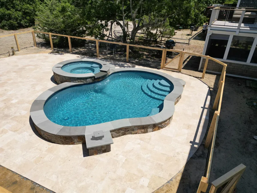 Aerial view of a freeform pool with an attached spa and travertine deck