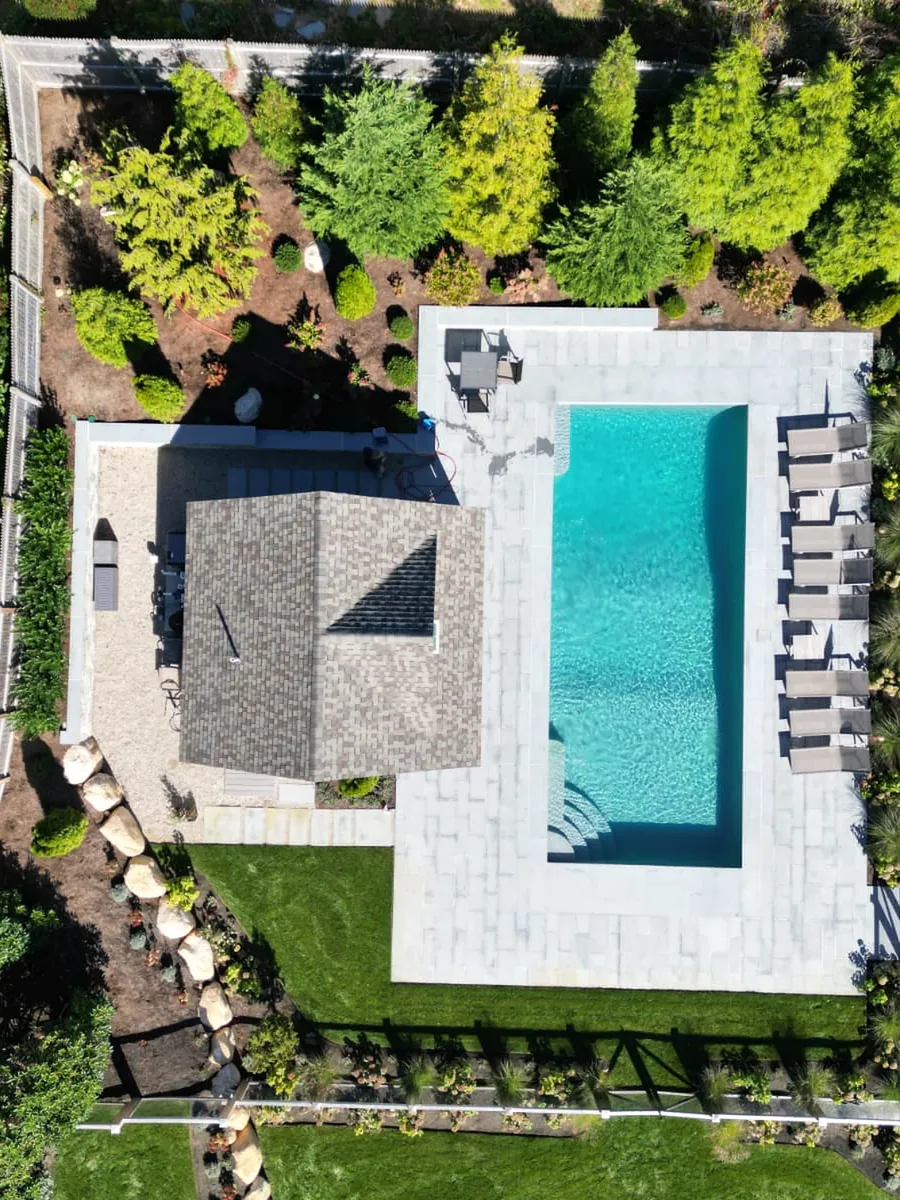 Aerial view of a pool with a pool house, loungers and landscaped beds