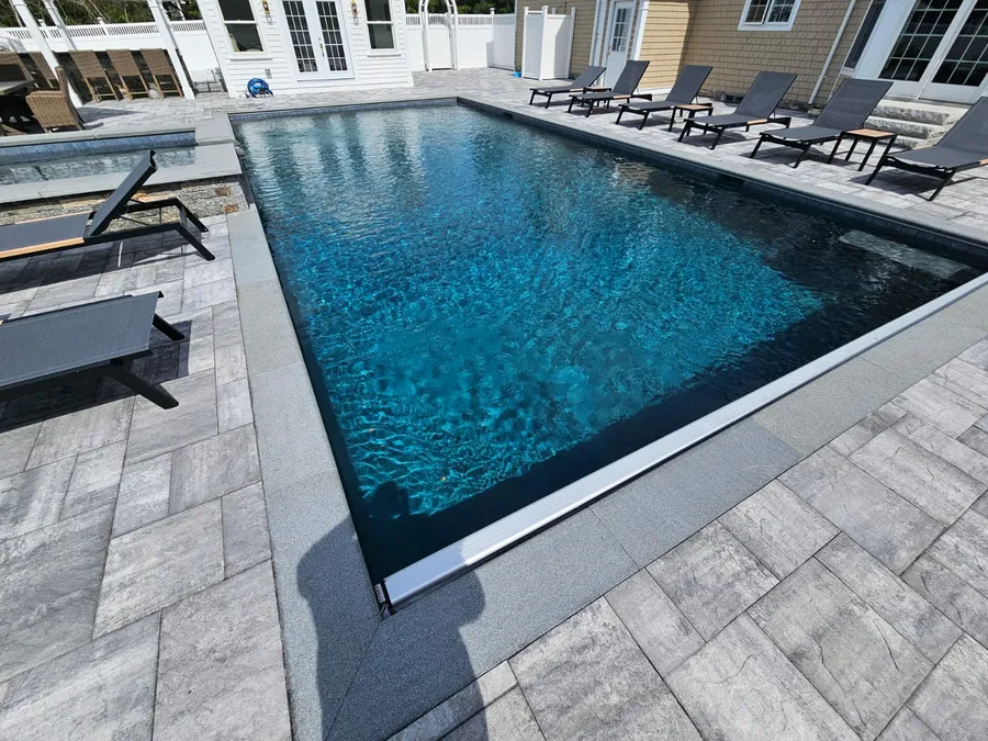 Pool with a dark liner, loungers and a grey paver deck