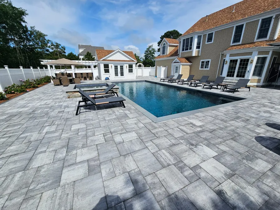 Rectangular pool on a large grey paver patio behind the house