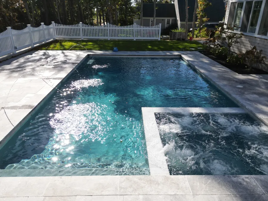 Raised spa spilling into a new pool with a light grey paver coping